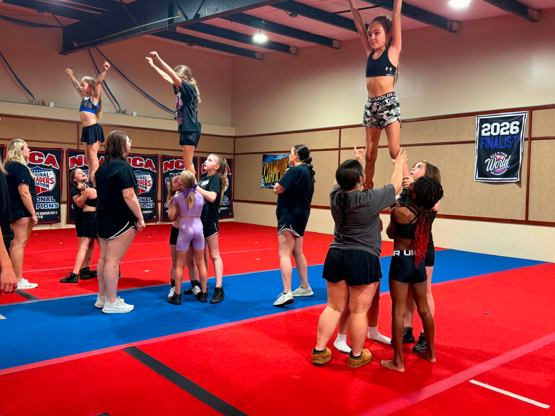 Cheer Pitt athletes practicing stunts in the gym while coaches spot.
