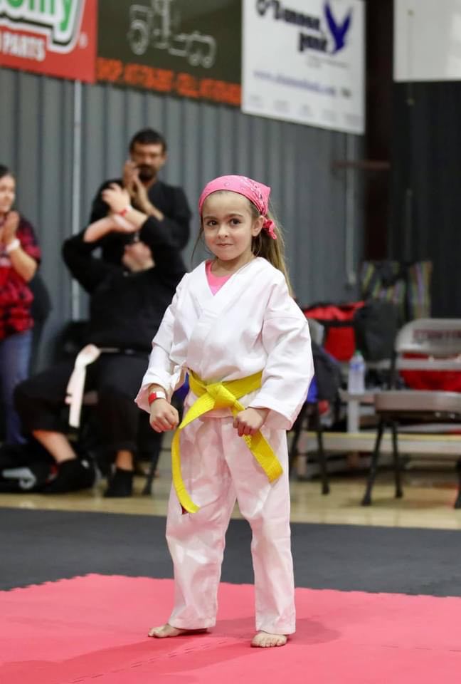 A young Elite Martial Arts athlete in a white gi and yellow belt standing ready in a fighting stance on the competition mats.