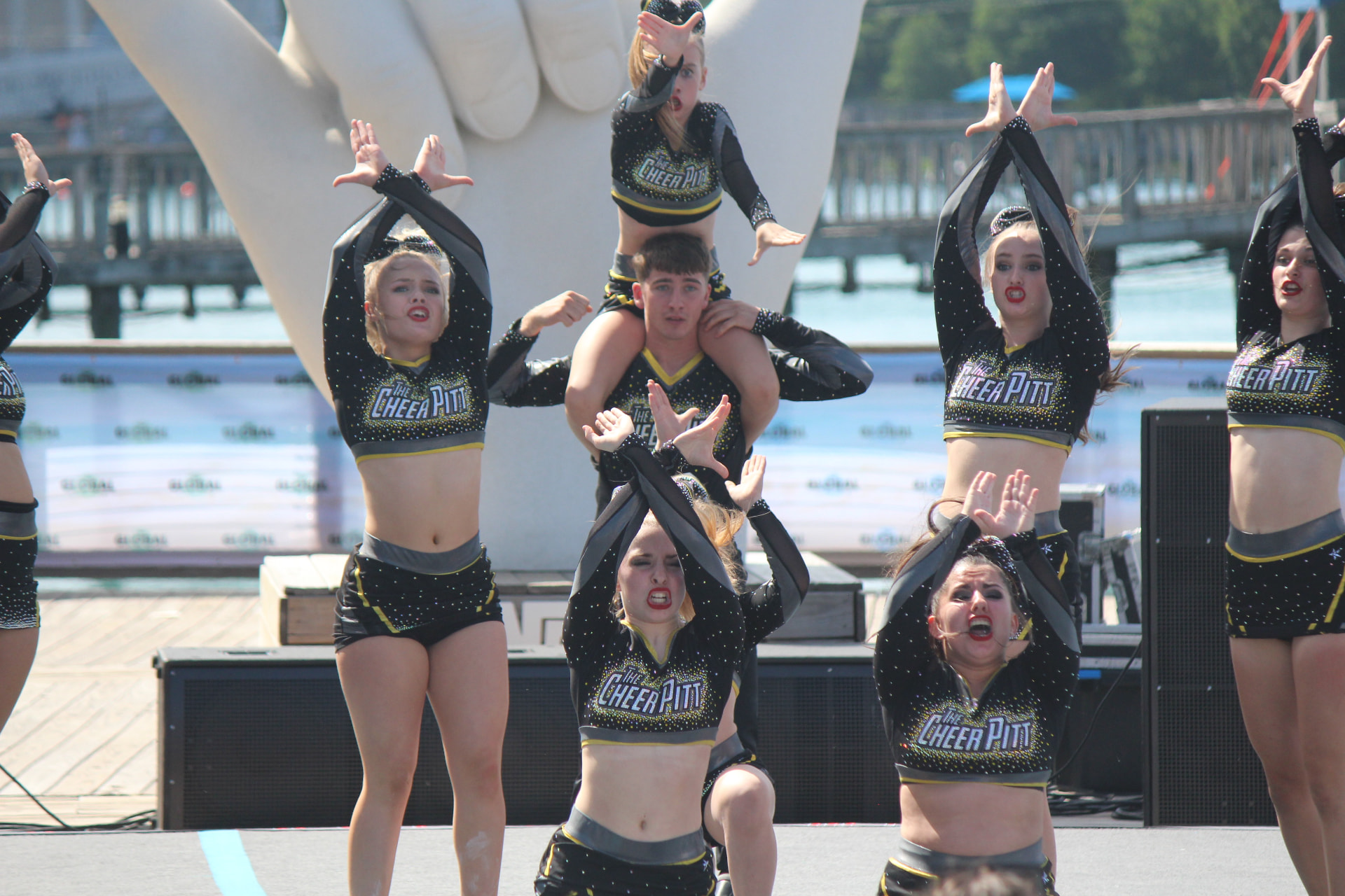 The Cheer Pitt squad performing a stunt outdoors, a flyer held on a teammate's shoulders while the rest of the team poses around her.