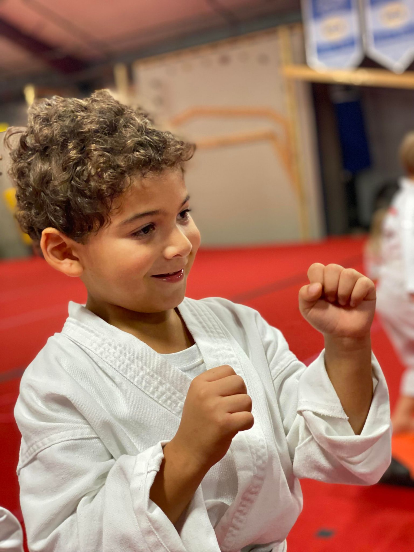 A smiling young athlete in a white uniform with both hands up in a martial arts stance.