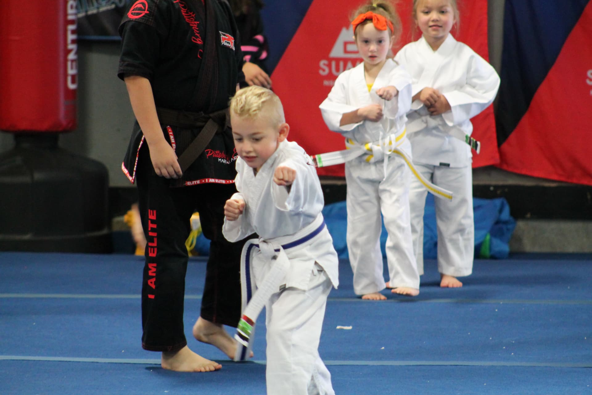 A young athlete practicing a punch in class as a coach in black and other students train nearby.
